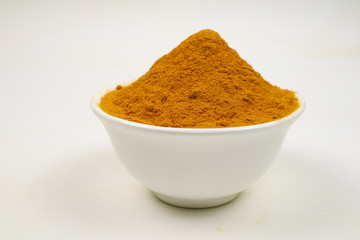 Turmeric powder in a separate white cup on a white background is used as a tonic for the body and food ingredients.