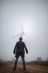 man standing and looking at a wind turbine in the fog