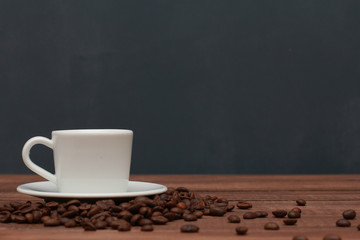 White cup of coffee on brown wooden table with scattered beans on dark blue wall background. Closeup, copy space, side. Coffee shop, cafe, morning, breakfast, drink  concept