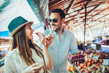 Young couple buying fruits and vegetables in a market on a sunny morning.