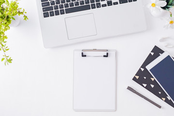 Flat lay blogger or freelancer workspace with a laptop, spring flowers, office supplies on a light background