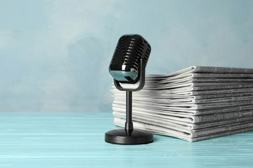 Newspapers and vintage microphone on light blue wooden table. Journalist's work