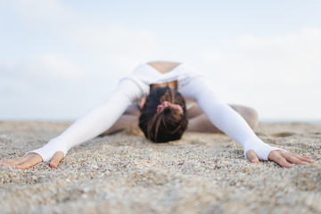 Fit girl doing yoga in the beach by the sea on a sunny day