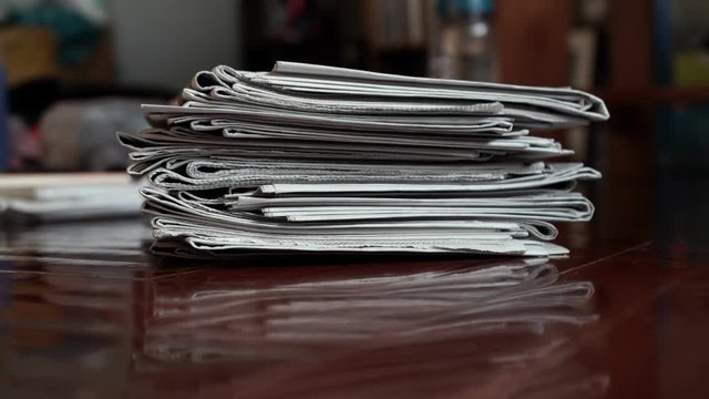 A pile of newspaper moving into the middle of frame by hand