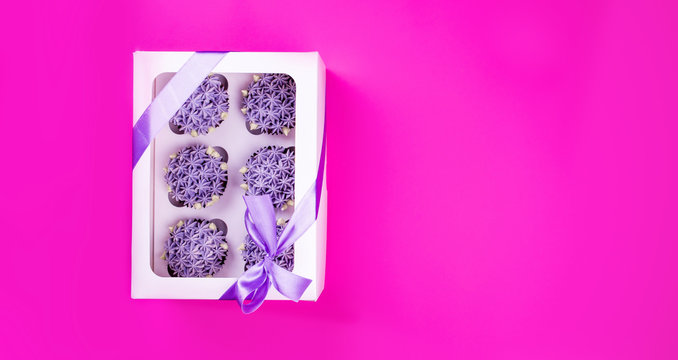 Delicious shawn cupcakes with curd cream in the form of flowers on a pink background.