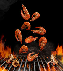 Falling down barbecue bbq grilled shrimps with halves of garlic, black background. Flaming fire, ember charcoal. Prawns, seafood, shellfish. Close up