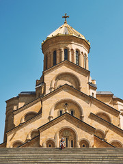 Tourist girl sitting in front of Holy Trinity Cathedral of Tbilisi Sameba on a sunny day, vertical