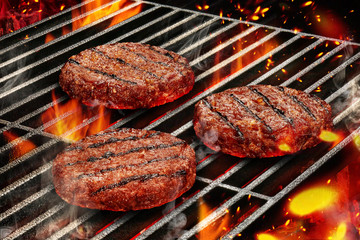 Grilling process of preparing pork cutlets for burgers. Meat roasted on metal barbecue BBQ grill with bright flaming fire and ember charcoal. Close up - obrazy, fototapety, plakaty