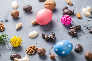Chocolate in the shape of eggs and rabbits with bright Easter eggs on a gray background. Festive spring greeting card