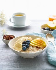 Whole oatmeal, large bowl of porridge with banana, blueberries, apple, nuts. Side view, vertical
