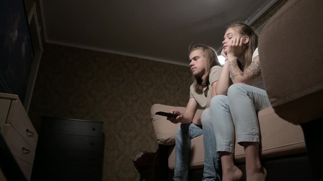 Young couple is watching tv. Woman switches channels, man selects control.