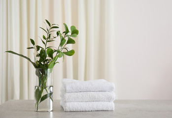 Fototapeta na wymiar Fresh towels and green branches on light grey stone table in bathroom