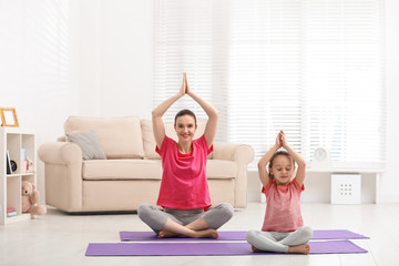 Young mother with little daughter practicing yoga at home