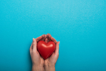 Fototapeta premium Top view of decorative red heart in woman hands on blue background, world health day concept