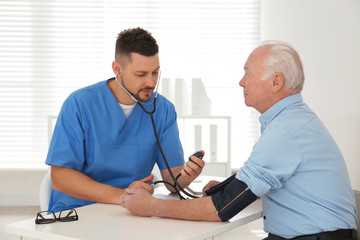 Doctor measuring blood pressure of senior patient in office