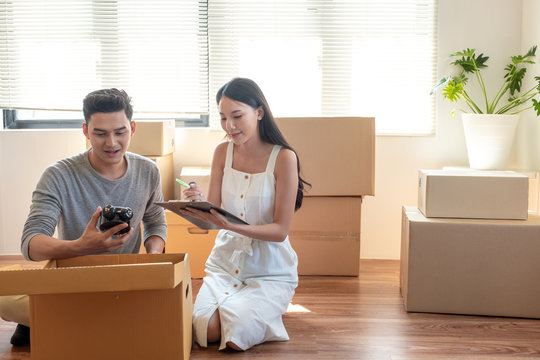Young Asian married couple helping unpacking and checking items together and woman checking stuff by using checklist
