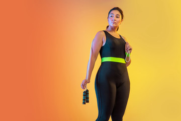 Young caucasian plus size female model's training on gradient orange-peach background in neon...