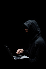 hacker in hood and mask pointing with finger at laptop isolated on black