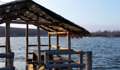 A wooden gazebo floats on a river. A house on the water