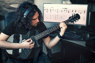 long haired rock composer musician man with headphones play electric guitar with musical score on...
