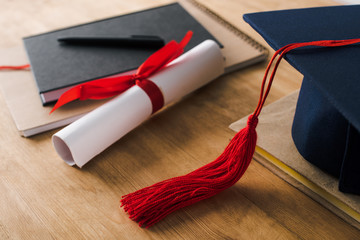 Selective focus of notebooks, pen, diploma and graduation cap with red tassel on wooden background