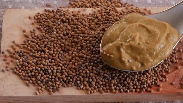 Mustard in a spoon, next to the mustard seeds sprinkled on a wooden board. Seasonings