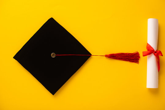 Top view of diploma and graduation cap with red tassel on yellow background