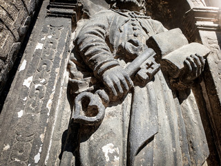 Closeup image of ancient stone sculpture of priest holding a book and key