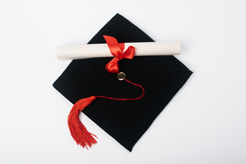 Top view of black graduation cap with red tassel and diploma on white background