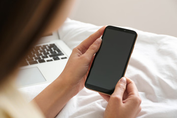 Young woman using modern smartphone on bed at home, closeup