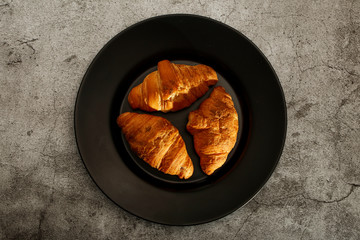 Fresh croissants in a black plate on a black background, close-up top view.