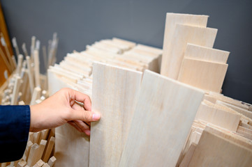 Male hand designer choosing beige balsa wood plank in stationery shop. Wooden material for making...