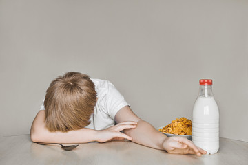 The boy sits at the table and doesn 't want to eat breakfast. Tired of useful food. Moves away from himself a plate of flakes and milk. © Илья Мышенков