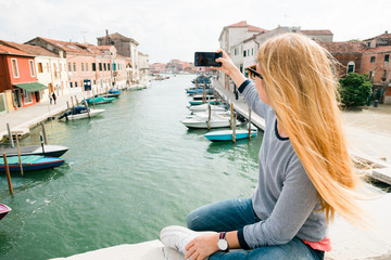 Fototapeta na wymiar Young woman taking a phone on the bridge in Murano in Venice, Italy