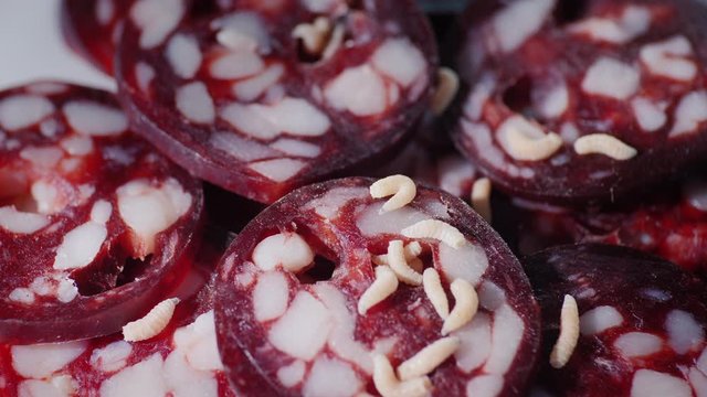 The maggots crawl on the spoiled sausage, disgusting unsanitary