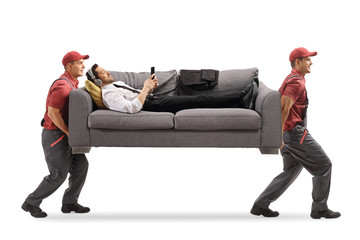 Two movers carrying a man with headphones on a sofa