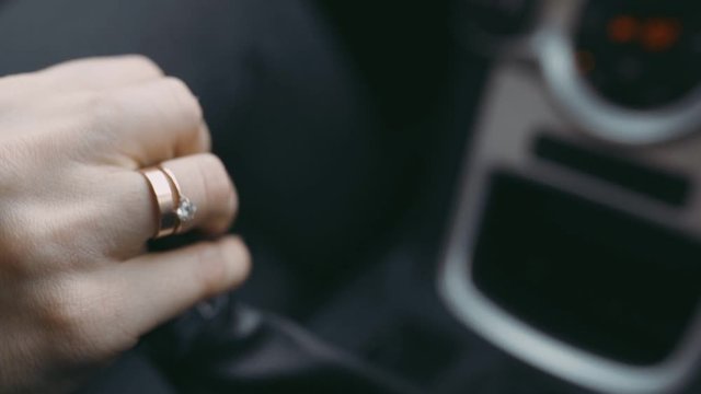 Married girl hand controls a manual gearbox, shifts gears in car. Close-up of woman's hand in jacket sitting in the car. The hand of a modern girl with an engagement ring on her finger, slow motion.