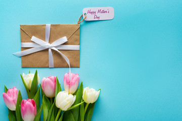 Top view of envelope with happy mothers day lettering on paper label and tulips on blue background