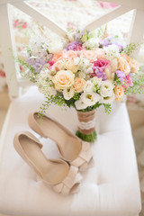 The bride’s wedding bouquet of different flowers, together with wedding shoes, stands on a white chair.