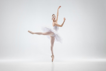 Naklejka na ściany i meble Graceful classic ballerina dancing isolated on white studio background. Woman in tender clothes like a white swan characters. The grace, artist, movement, action and motion concept. Looks weightless.