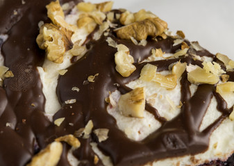 Very strong closeup on a cake with white mass and nuts covered with chocolate, a delicious caloric coffee snack, visible dough structure