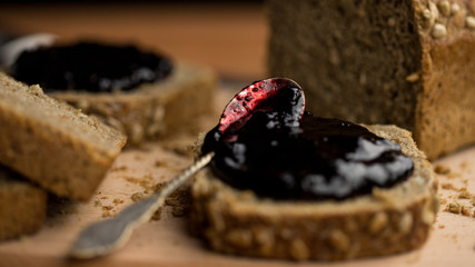 Antique spoon dirty from jam lying on a slice of bread surrounded by bread, warm light and a wooden table