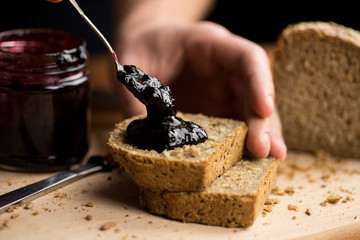 Person applying blueberry jam on fresh slices of bread, close-up of the moment when the jam touches...