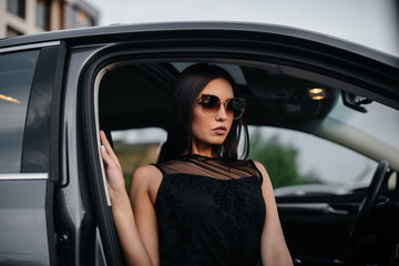 Plakat Stylish young girl sitting in a business class car in a black dress. Business fashion and style