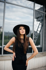 Stylish young and sexy girl posing in front of a business center in black. Fashion and style