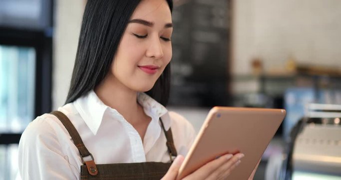 Female barista using tablet to assist her work at coffee shop. An attractive girl works on a tablet with smile.