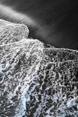 Beach with black volcanic sand and wave foam on the coast of Bali