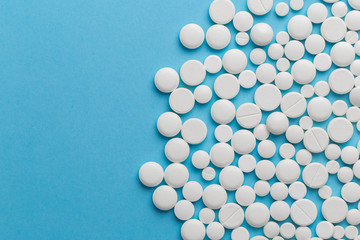 scattered white pills on a blue table. Layout for special offers such as advertising or other ideas. The concept of medicine, pharmacy and healthcare. Space for copy. flat lay for text or logo.
