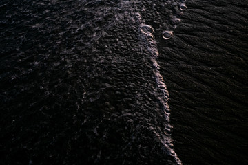 Beach with black volcanic sand and wave foam on the coast of Bali