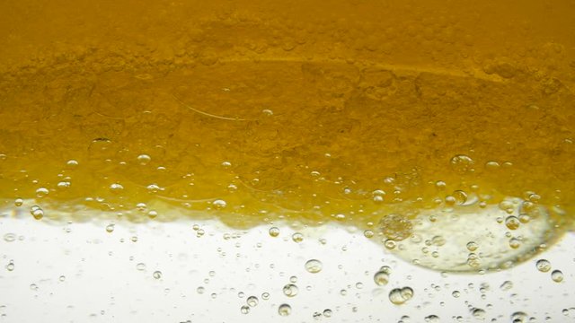 Close-up view of mixing linseed and sesame oil shooting on a white background in research lab. Focus boiling yellow peanut oil spread widely bubble texture full frame and macro many various droplets.